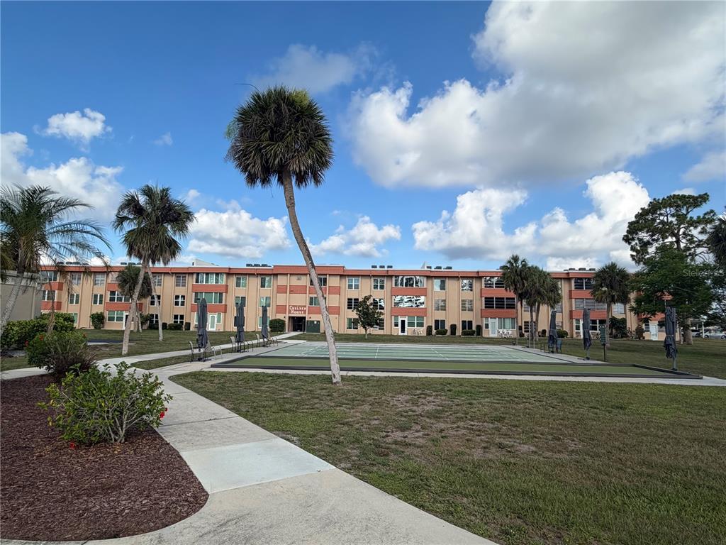 A multi-story apartment building features a shuffleboard court and palm trees in the foreground — 2290 AARON STREET UNIT 101, PORT CHARLOTTE, FL