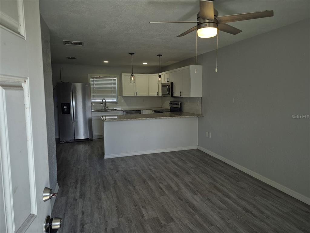 A kitchen with white cabinets, stainless steel appliances, and a breakfast bar overlooks a room — 321 JERU BOULEVARD UNIT C, TARPON SPRINGS, FL