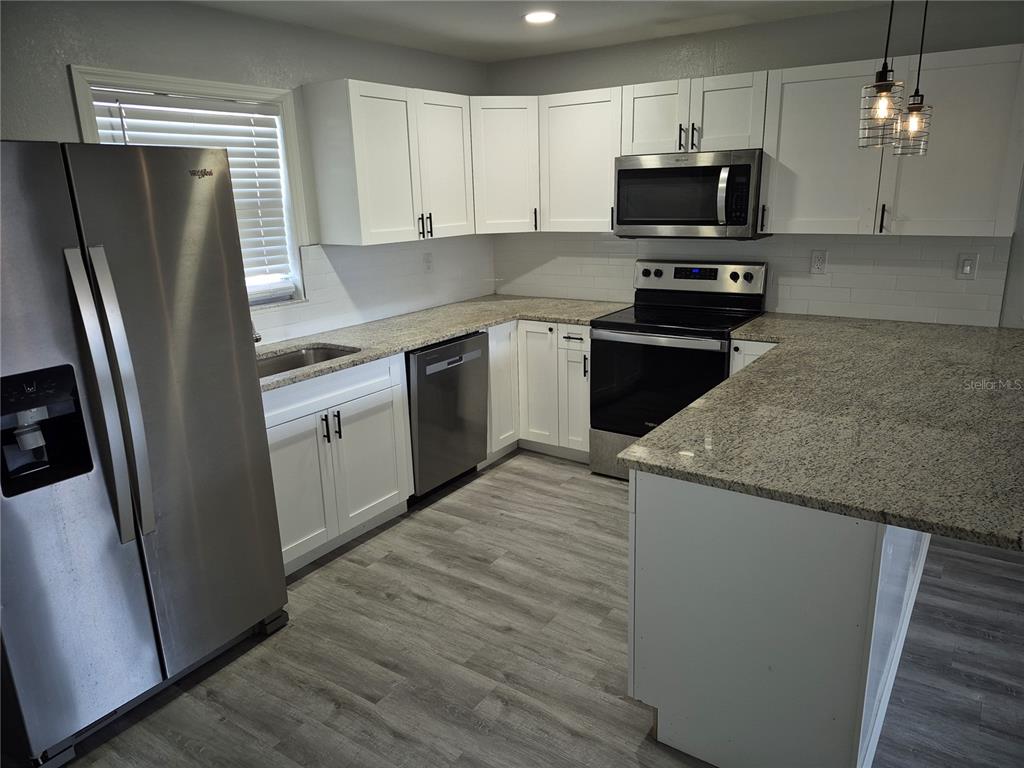 A kitchen features white cabinets, granite countertops, stainless steel appliances, and light wood-look flooring — 321 JERU BOULEVARD UNIT C, TARPON SPRINGS, FL