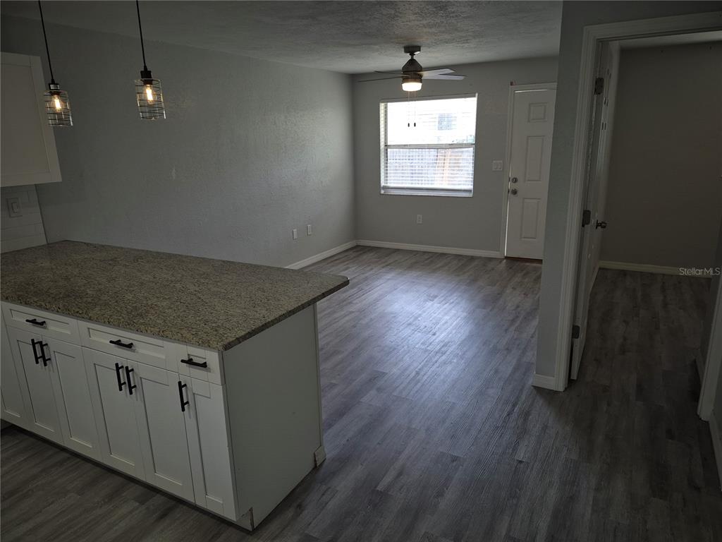 A kitchen island with granite countertops overlooks an open living area with wood-look flooring — 321 JERU BOULEVARD UNIT C, TARPON SPRINGS, FL