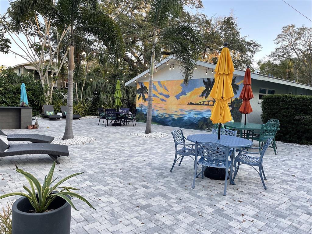 A paved outdoor patio features dining sets, lounge chairs, and a large sunset wall mural — 1912 MORRILL UNIT Lime, SARASOTA, FL