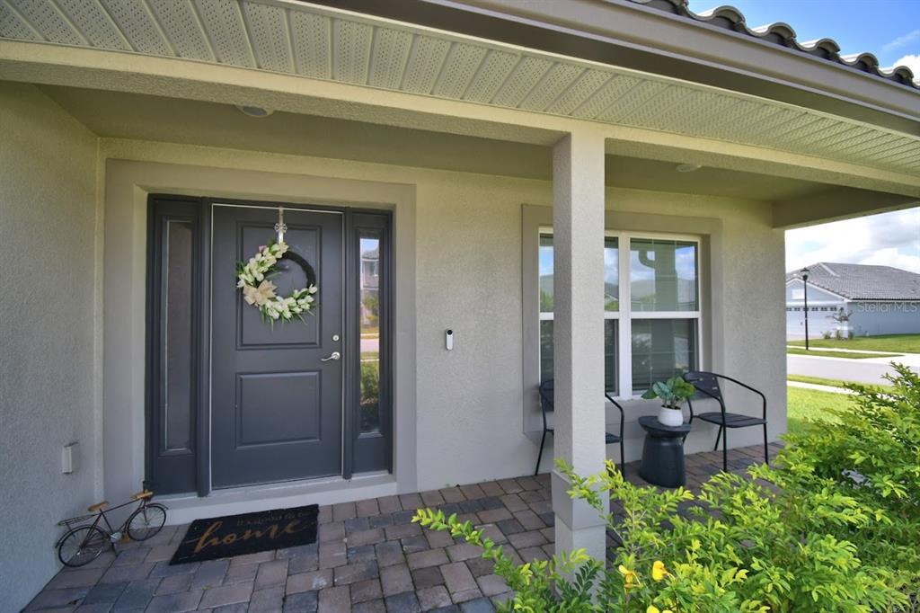 A covered front porch with a gray door, a wreath, and two chairs on pavers — 4669 GRANDVIEW GLEN DRIVE, AUBURNDALE, FL
