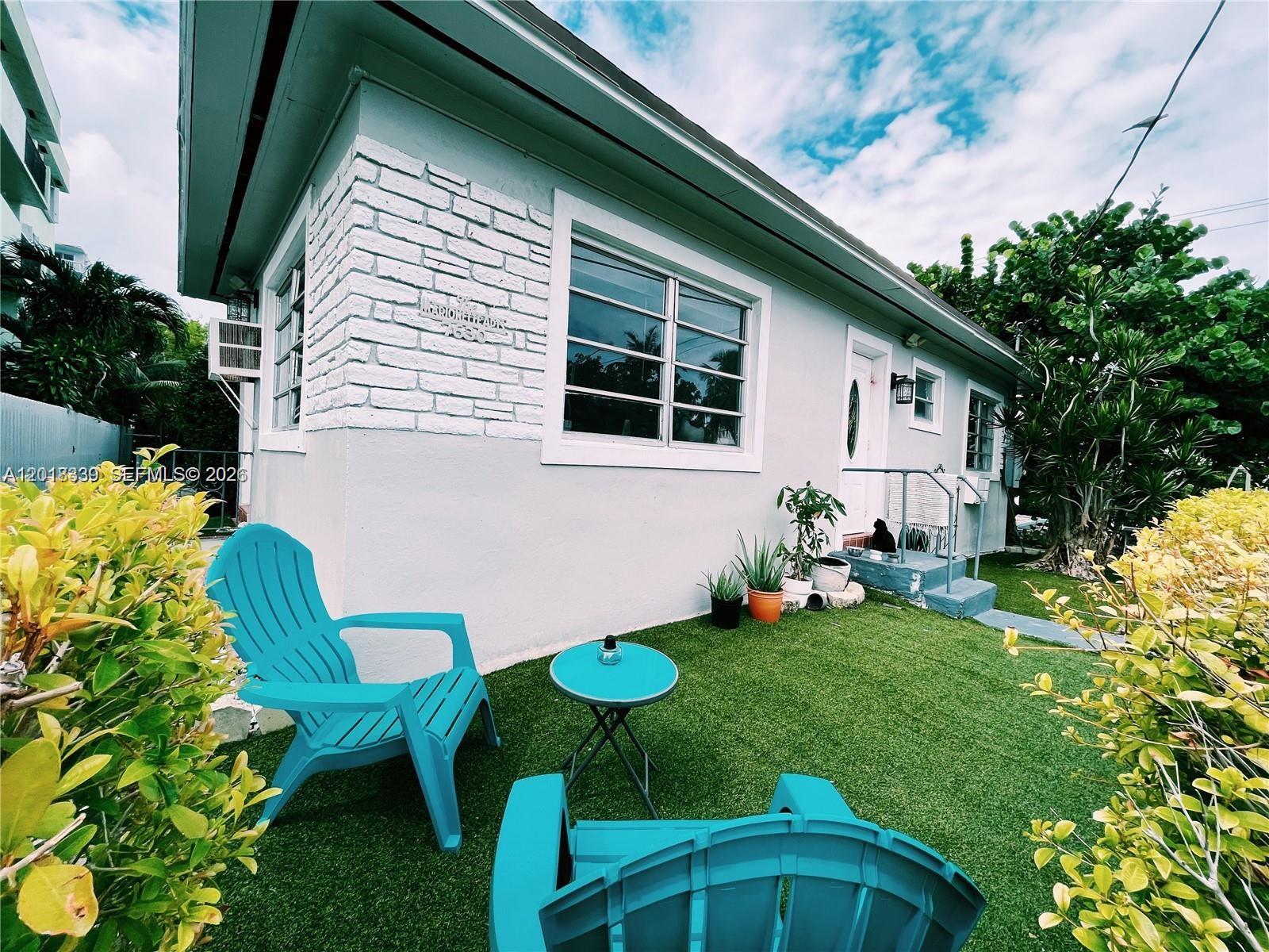 A light-colored house with a brick corner, turquoise chairs, and artificial grass in the yard — 7630 Byron Ave, Miami Beach FL 33141, MIAMI BEACH, FL