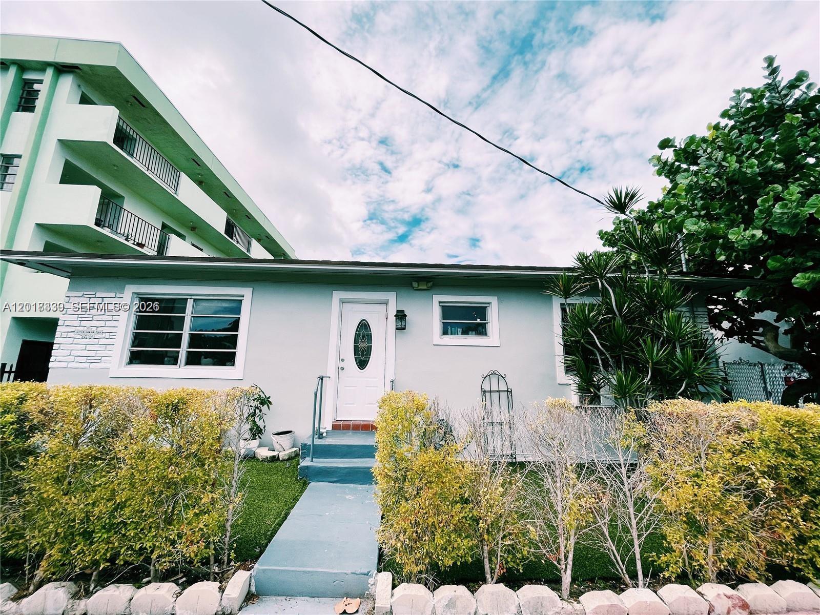 A light-colored single-story house features a white front door, a walkway, and manicured hedges — 7630 Byron Ave, Miami Beach FL 33141, MIAMI BEACH, FL