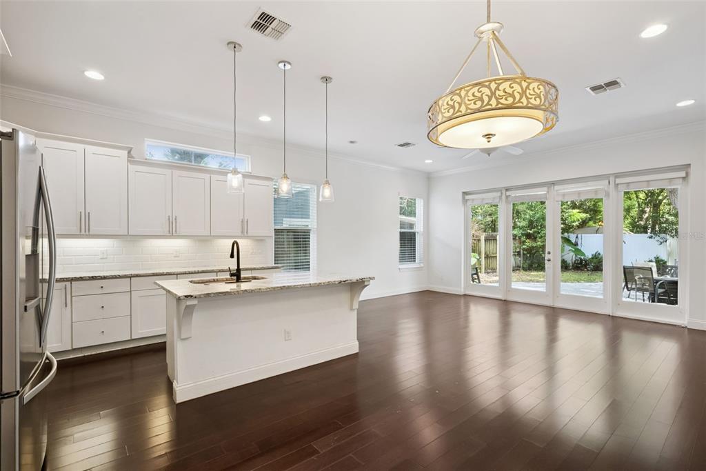 A white kitchen with an island and dark wood floors opens to a backyard patio — 2505 DEPAUW AVENUE, ORLANDO, FL