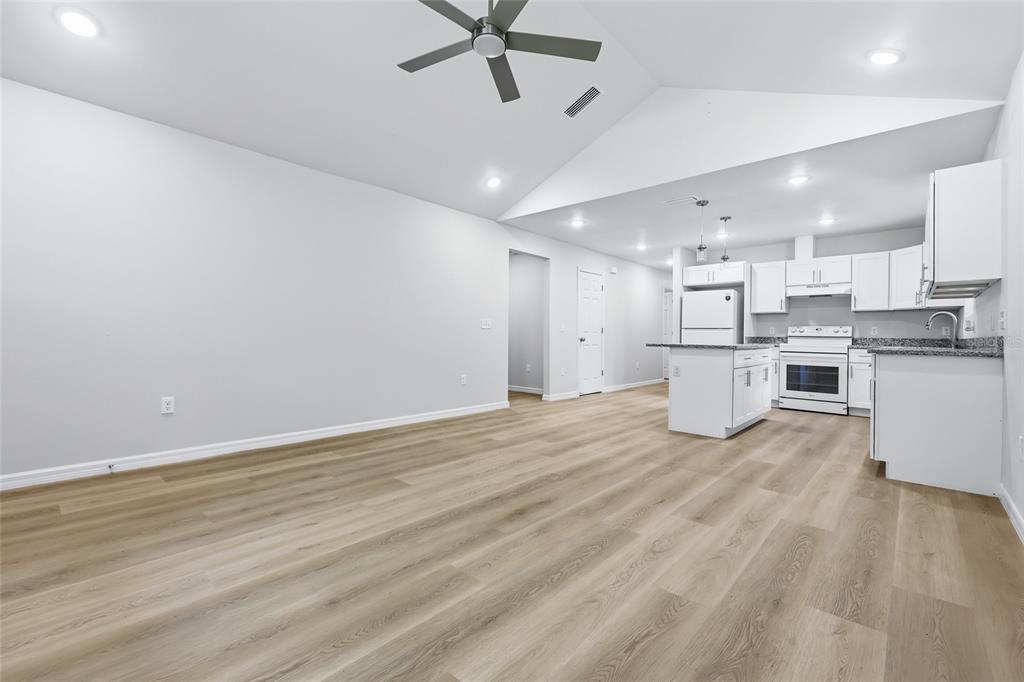 A bright, open-concept living area features light wood-look flooring, vaulted ceilings, and a white kitchen — 925 NE 19TH STREET, GAINESVILLE, FL