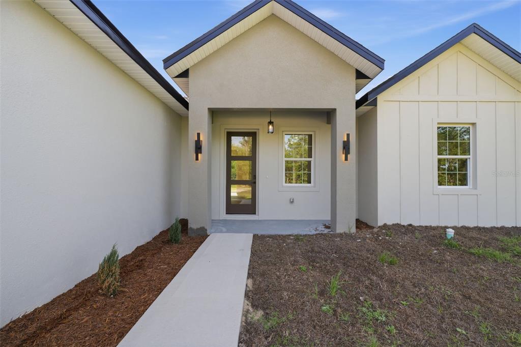 The exterior of a modern home features a covered entryway, a glass-paneled door, and siding — 7433 SW 138TH TERRACE, DUNNELLON, FL