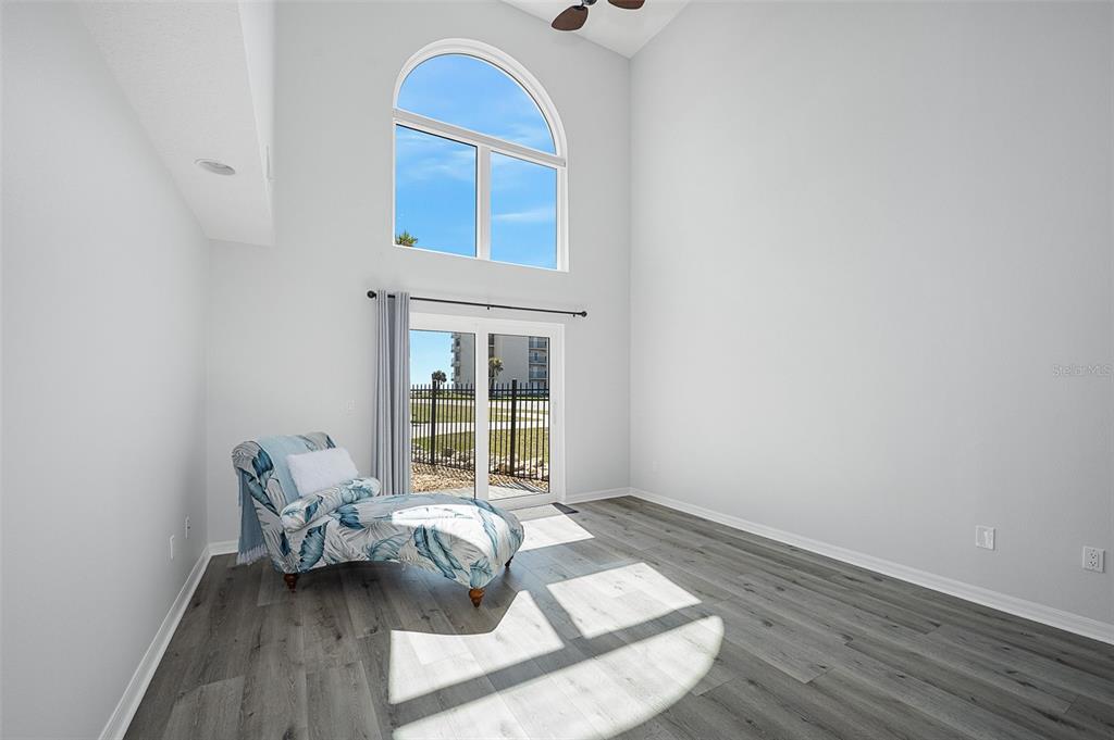 A bright living room features high ceilings, gray wood-look flooring, and a large arched window — 5 SUNNY BEACH DRIVE, ORMOND BEACH, FL