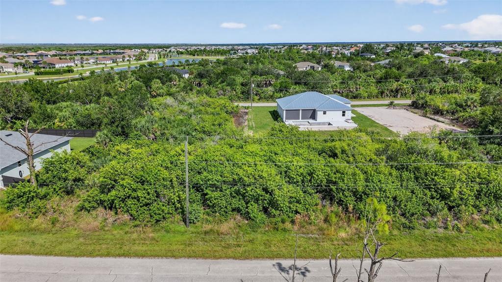 An aerial view shows a vacant, wooded lot situated next to a modern single-family home — 8044 THRUSO ROAD, PORT CHARLOTTE, FL