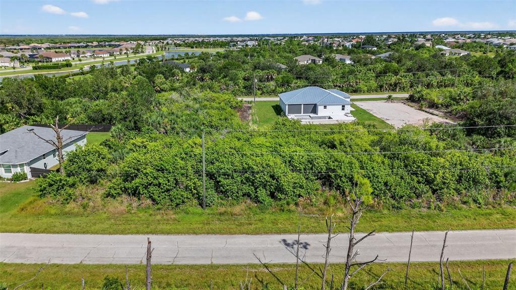 An aerial view shows a single-story house surrounded by dense vegetation and a paved road — 8044 THRUSO ROAD, PORT CHARLOTTE, FL