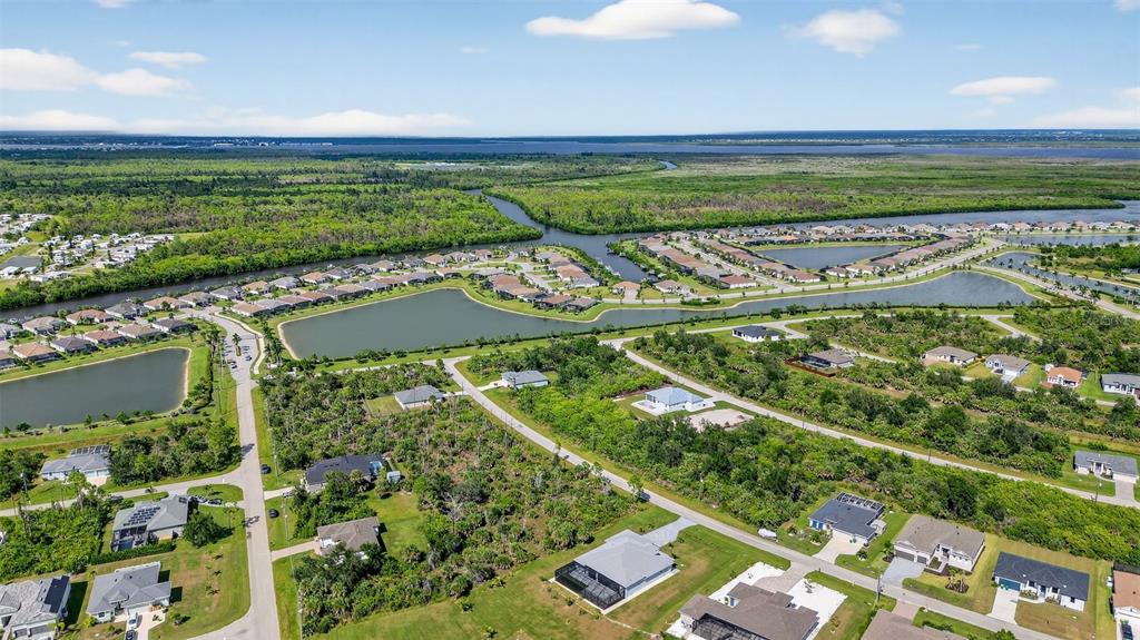 An aerial view shows a suburban neighborhood with houses, ponds, and surrounding natural vegetation — 8044 THRUSO ROAD, PORT CHARLOTTE, FL