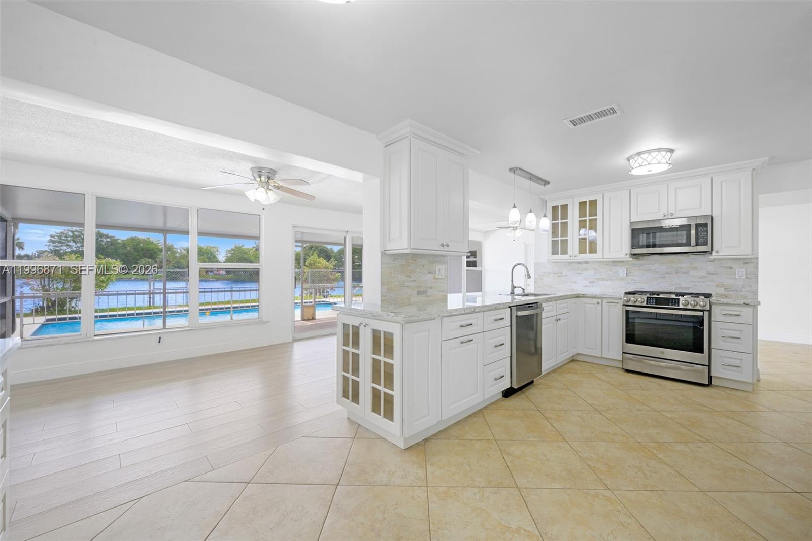 A bright kitchen with white cabinets and stainless steel appliances overlooks a pool and lake — 2320 NW 73rd Ave, Sunrise FL 33313, SUNRISE, FL