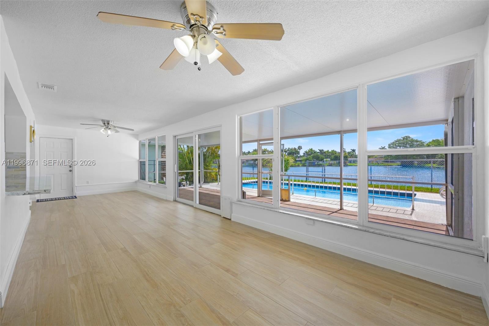 A bright living room features light wood-look flooring, ceiling fans, and large windows overlooking a pool — 2320 NW 73rd Ave, Sunrise FL 33313, SUNRISE, FL