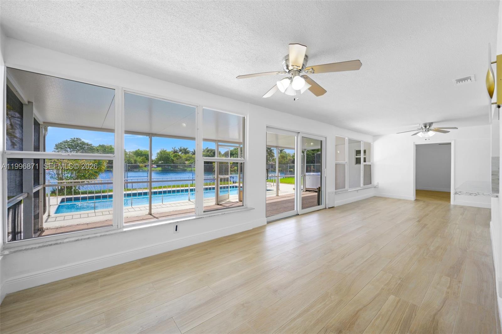 A bright, empty room with light wood-look flooring, ceiling fans, and large windows overlooking a pool — 2320 NW 73rd Ave, Sunrise FL 33313, SUNRISE, FL