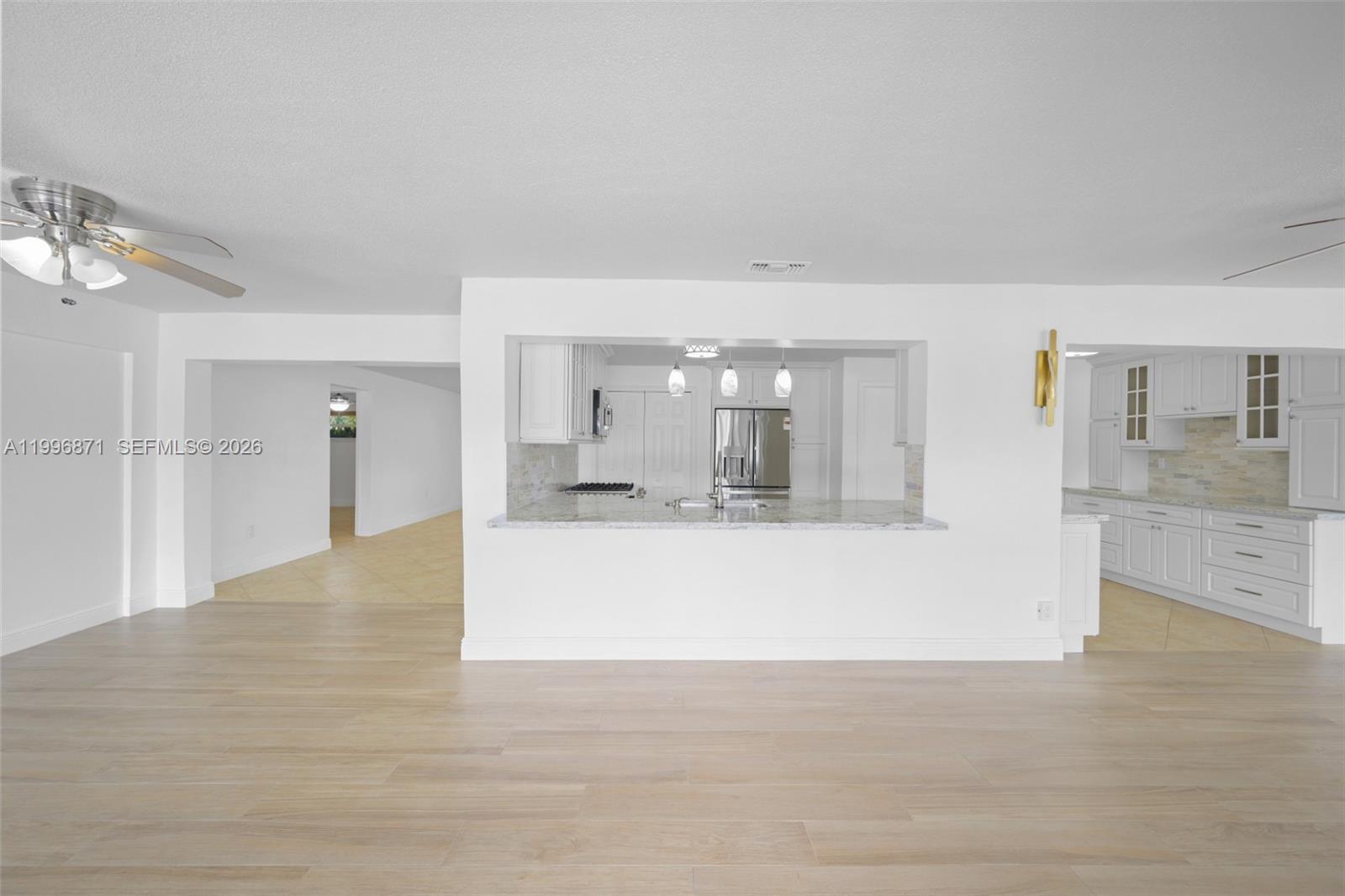 A kitchen with white cabinets and a pass-through window overlooks a light-floored living area — 2320 NW 73rd Ave, Sunrise FL 33313, SUNRISE, FL