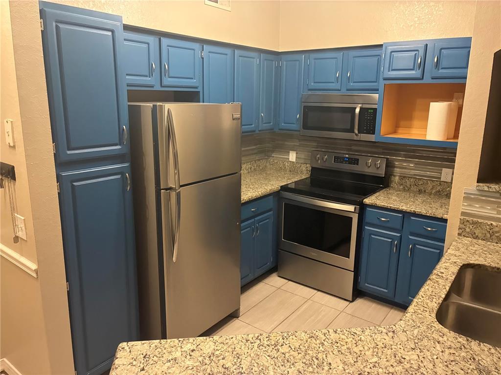 A kitchen features blue cabinets, stainless steel appliances, and speckled granite countertops — 3315 PARKCHESTER SQUARE BOULEVARD UNIT 206, ORLANDO, FL