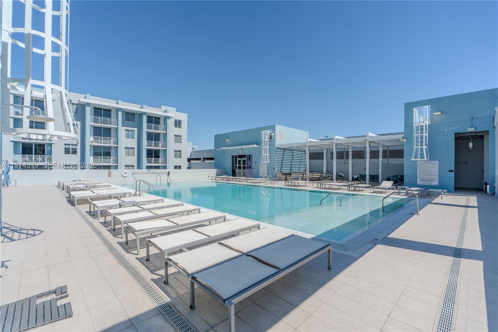 An outdoor swimming pool surrounded by lounge chairs on a tiled deck with blue buildings — 7751 NW 107th Ave # 721, Doral FL 33178, DORAL, FL