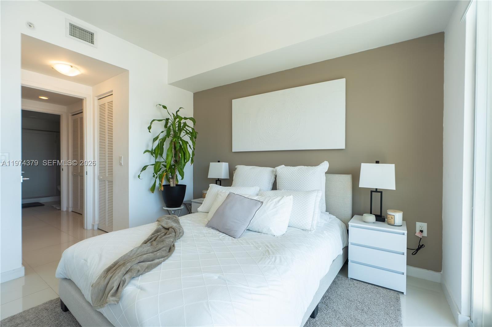 A bedroom features a bed with white bedding, a taupe accent wall, and a potted plant — 7751 NW 107th Ave # 721, Doral FL 33178, DORAL, FL