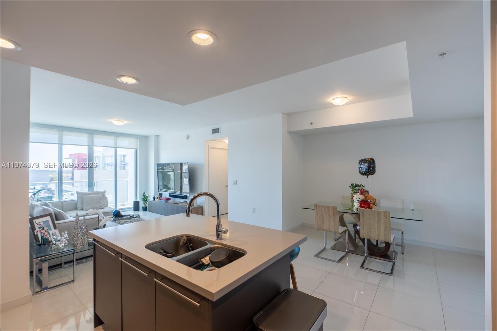 A modern kitchen island with a sink overlooks an open-concept living and dining area — 7751 NW 107th Ave # 721, Doral FL 33178, DORAL, FL