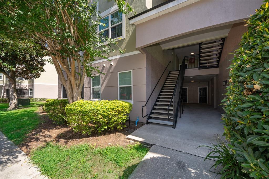 An exterior view of an apartment building entrance with stairs leading to an upper level — 6663 QUEENS BOROUGH AVENUE UNIT 101, ORLANDO, FL