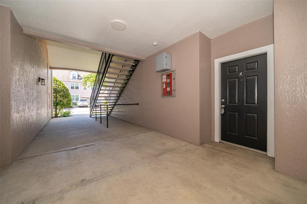 A ground-level apartment entrance features a black door, concrete flooring, and an outdoor staircase — 6663 QUEENS BOROUGH AVENUE UNIT 101, ORLANDO, FL