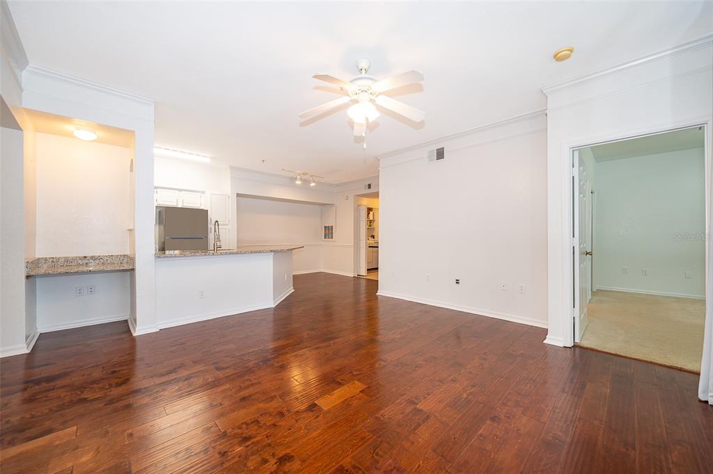 A living room with dark wood floors, a ceiling fan, and an open kitchen area — 6663 QUEENS BOROUGH AVENUE UNIT 101, ORLANDO, FL