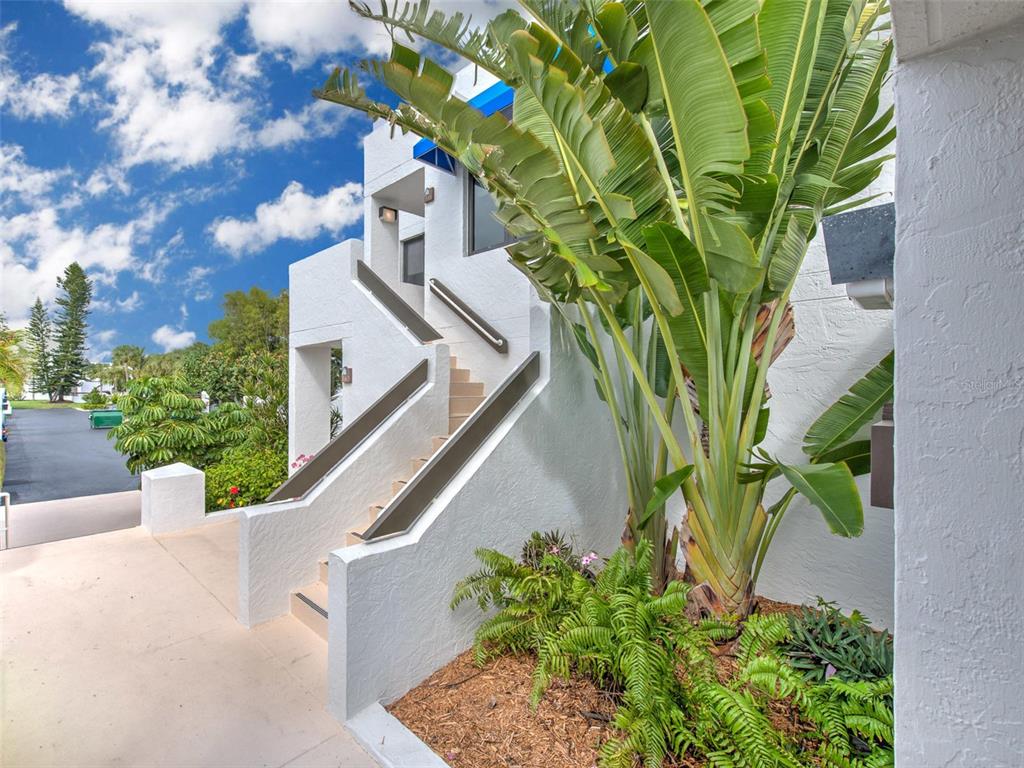 An exterior view of a white building featuring a staircase and large tropical plants — 741 BAYPORT WAY UNIT 741, LONGBOAT KEY, FL