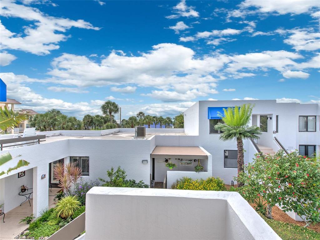 An elevated view of a white stucco building exterior with a palm tree and landscaping — 741 BAYPORT WAY UNIT 741, LONGBOAT KEY, FL