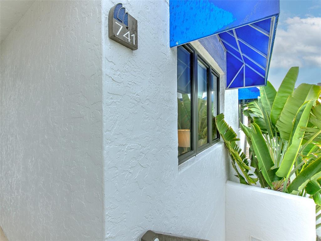A white stucco exterior wall features a house number plaque and a blue fabric awning — 741 BAYPORT WAY UNIT 741, LONGBOAT KEY, FL
