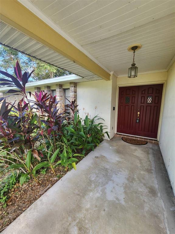 A concrete walkway leads to a covered entryway with double red doors and tropical landscaping — 549 BURLINGTON AVENUE NE, PALM BAY, FL