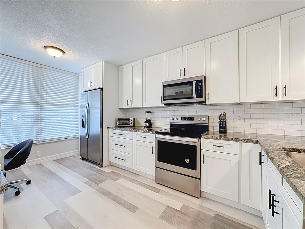 A kitchen with white cabinets, stainless steel appliances, granite countertops, and light wood-look flooring — 3750 PINEBROOK CIRCLE UNIT 107, BRADENTON, FL