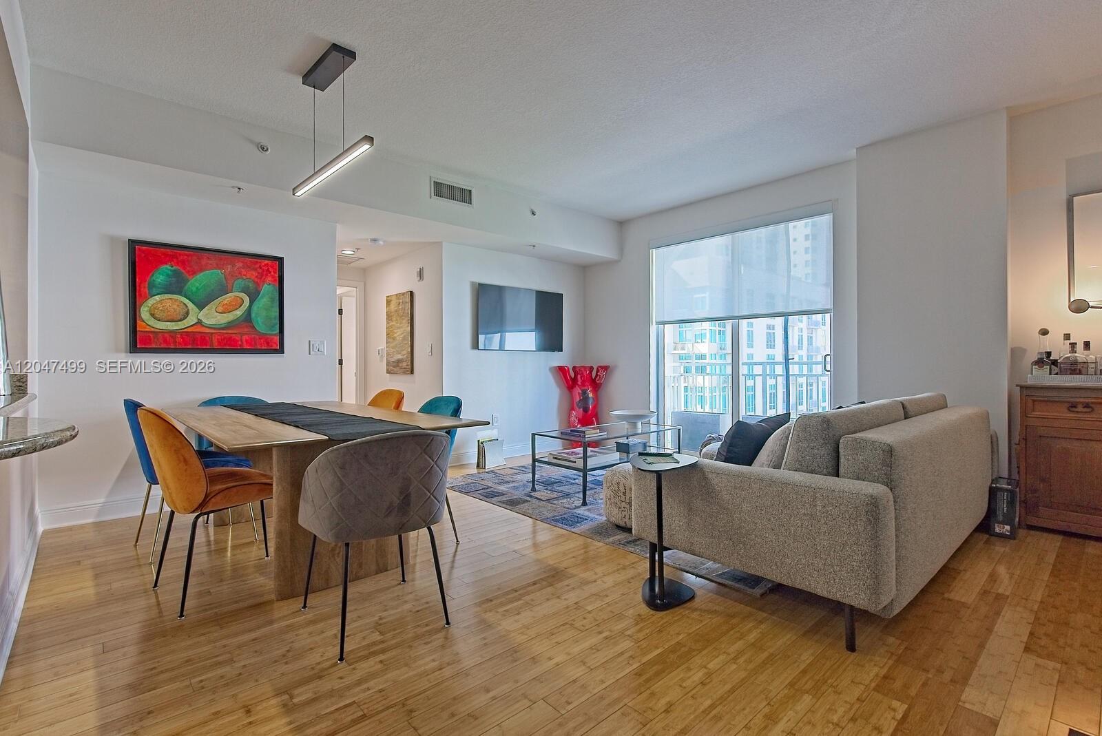 An open-concept living and dining area features hardwood floors, modern furniture, and a balcony view — 7285 SW 90th St # D613, Miami FL 33156, MIAMI, FL