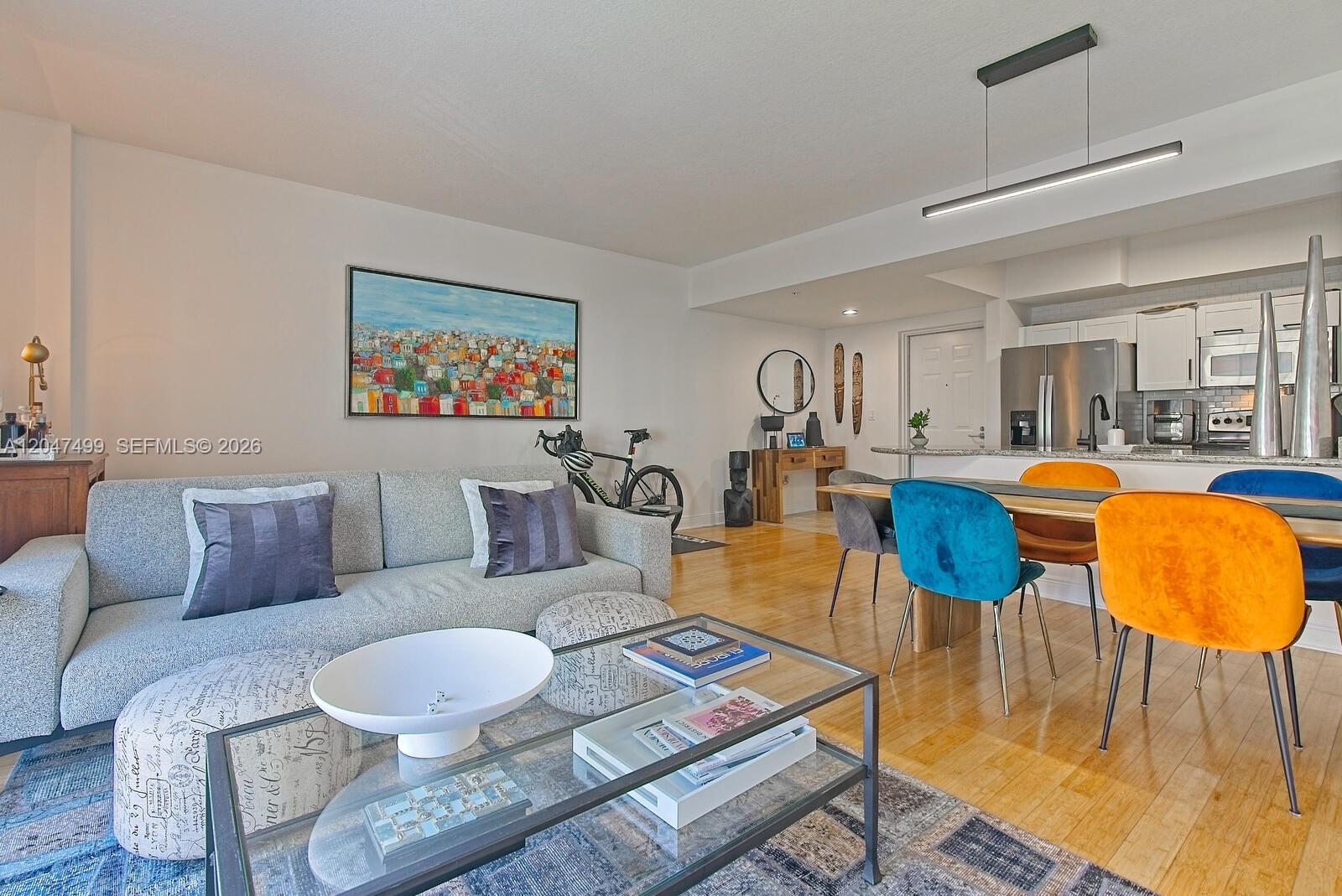 An open-concept living and dining area features a gray sofa, colorful chairs, and hardwood floors — 7285 SW 90th St # D613, Miami FL 33156, MIAMI, FL