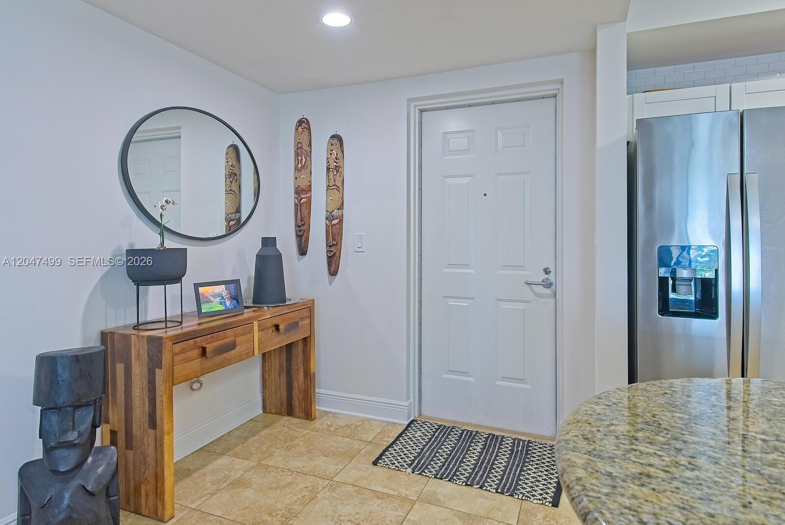 An entryway features a wooden console table, decorative wall masks, a mirror, and a door — 7285 SW 90th St # D613, Miami FL 33156, MIAMI, FL
