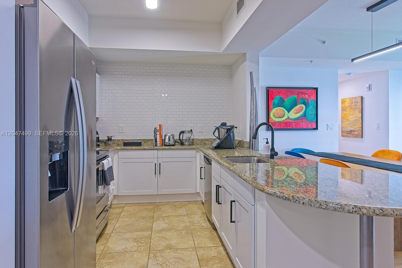 A kitchen features white cabinetry, granite countertops, stainless steel appliances, and a subway tile backsplash — 7285 SW 90th St # D613, Miami FL 33156, MIAMI, FL