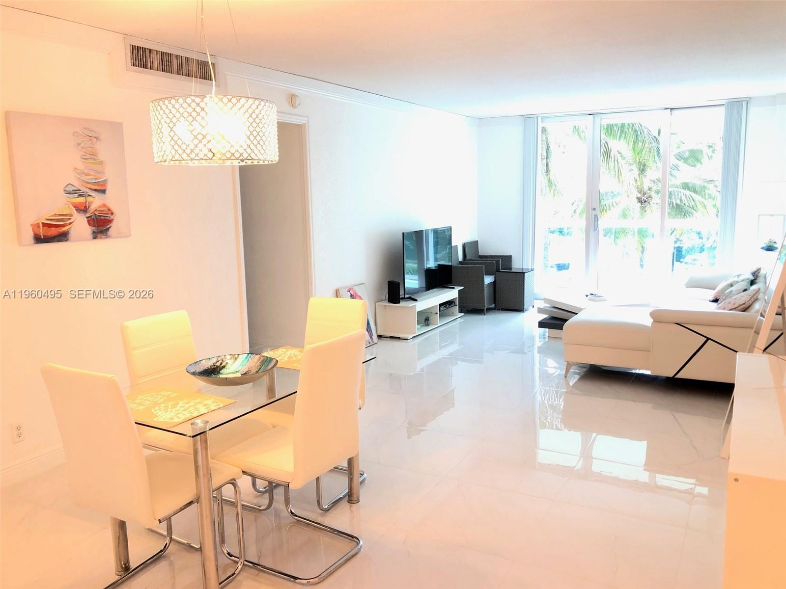 A bright living and dining area features white tile floors, modern furniture, and floor-to-ceiling windows — 3901 S Ocean Dr # 2J, Hollywood FL 33019, HOLLYWOOD, FL
