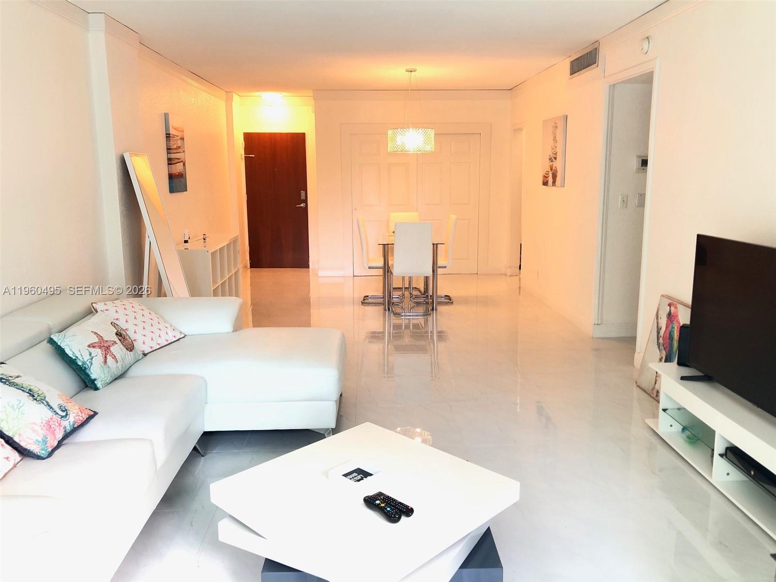 A living room and dining area feature white tile floors, white furniture, and a chandelier — 3901 S Ocean Dr # 2J, Hollywood FL 33019, HOLLYWOOD, FL