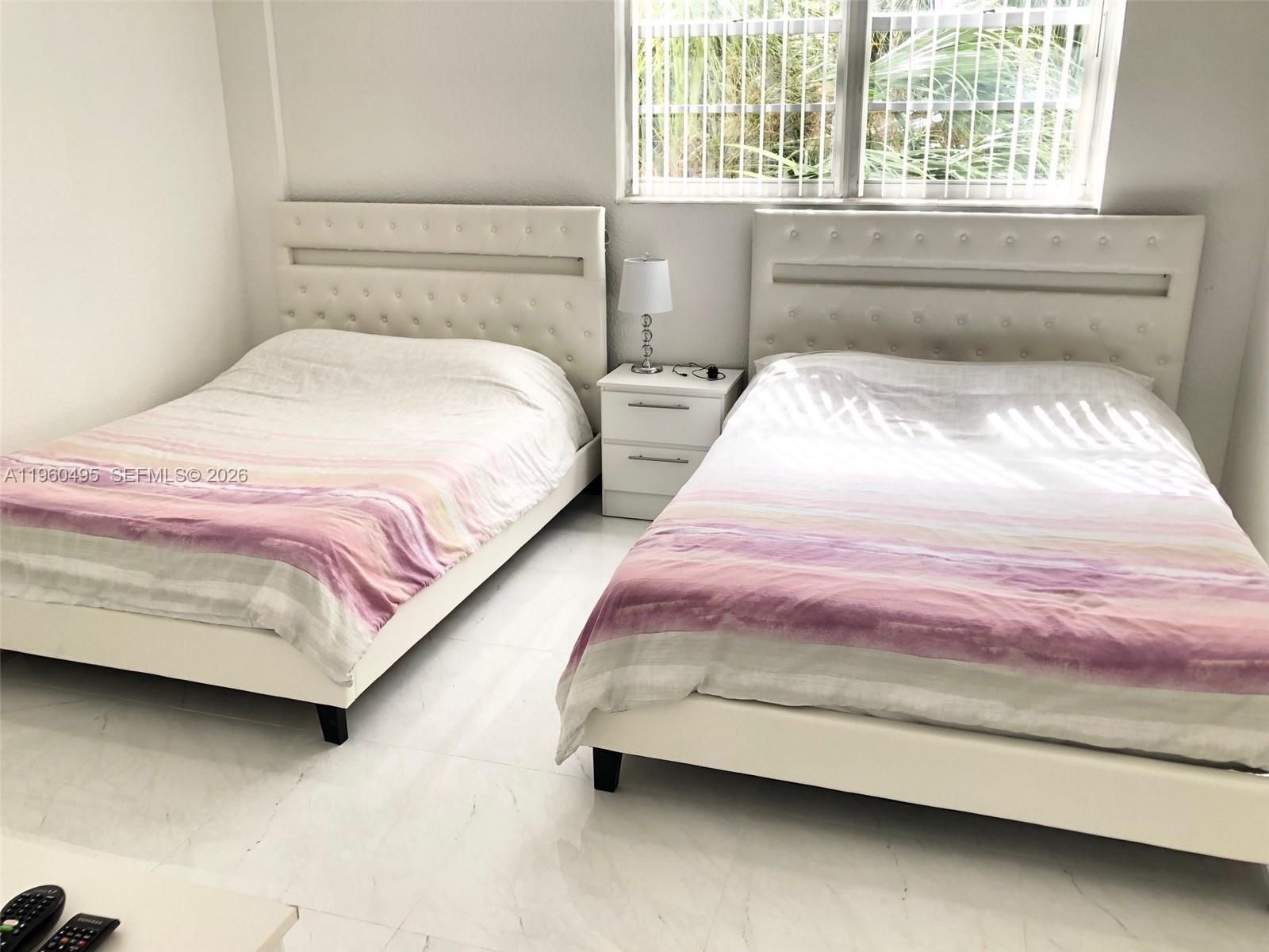 A bedroom features two white tufted beds with pink-striped bedding and a central nightstand — 3901 S Ocean Dr # 2J, Hollywood FL 33019, HOLLYWOOD, FL