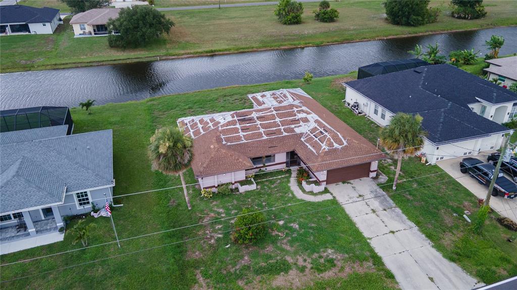 An aerial view shows a single-story house with a tarp covering its damaged roof — 273 ROTONDA CIRCLE, ROTONDA WEST, FL