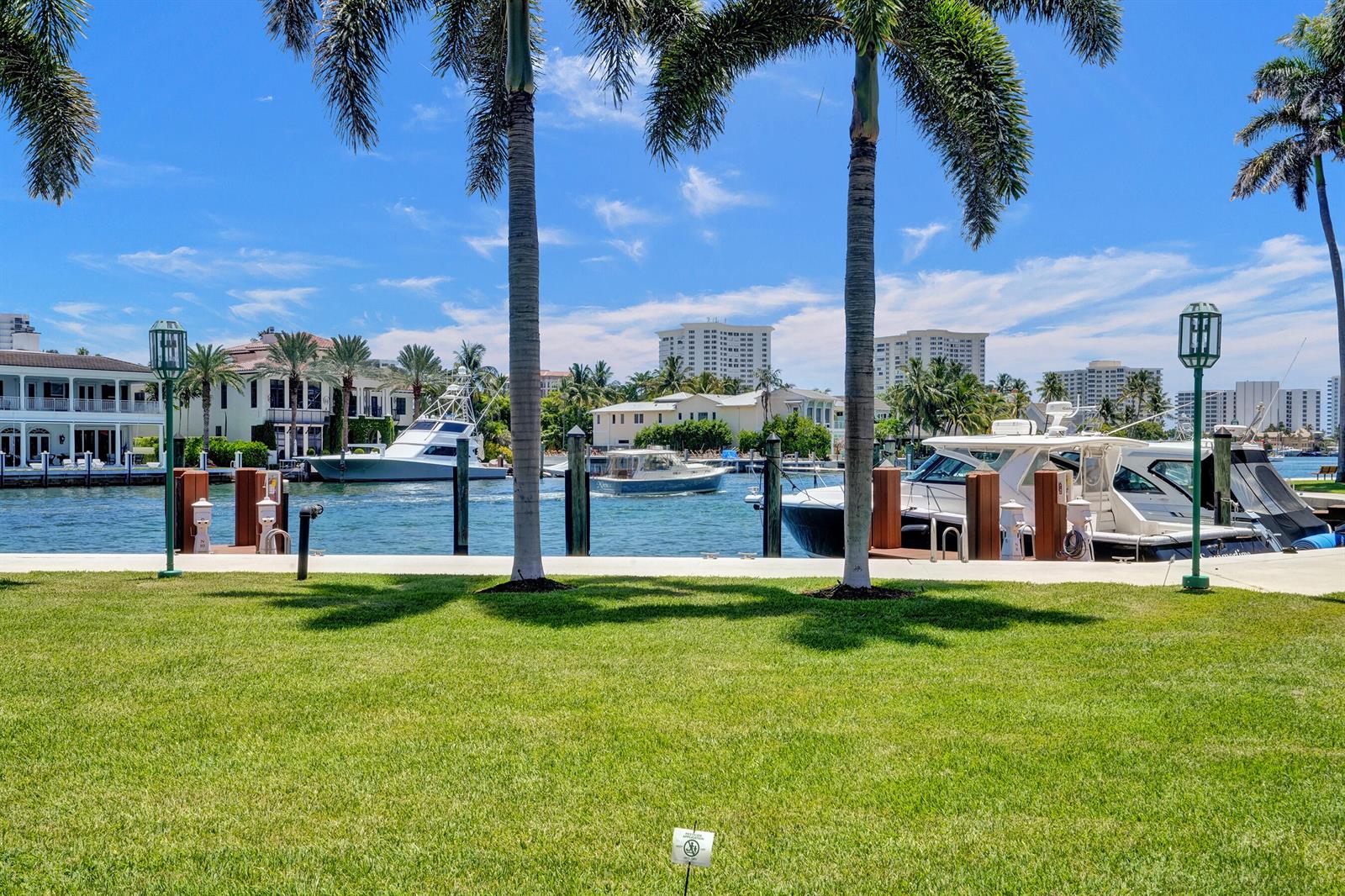 A grassy lawn overlooks a canal with docked boats and palm trees under a blue sky — 100 SE 5th Avenue # 406, Boca Raton FL 33432, BOCA RATON, FL