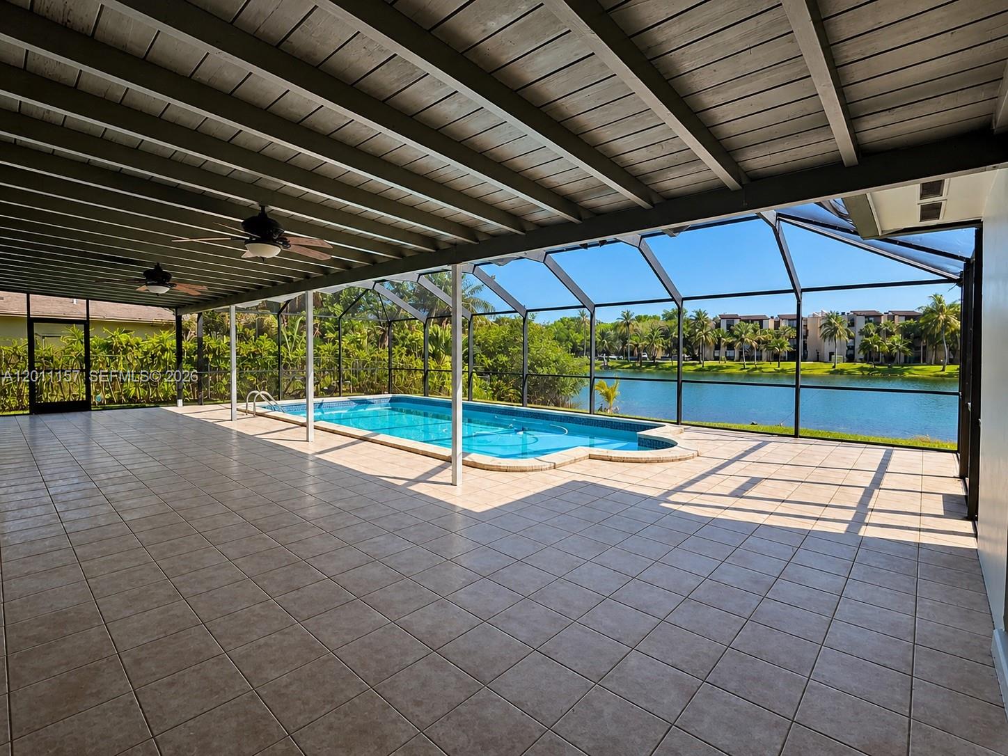 A screened-in patio with tile flooring overlooks a swimming pool and a lake — 14250 SW 85th St, Miami FL 33183, MIAMI, FL