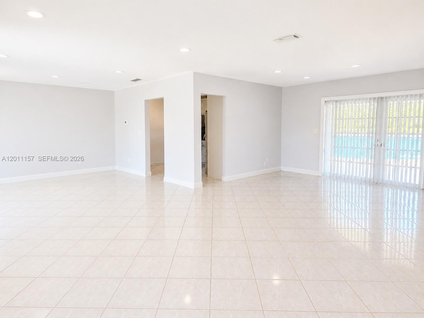 An empty room features light-colored tile flooring, white walls, recessed lighting, and sliding glass doors — 14250 SW 85th St, Miami FL 33183, MIAMI, FL
