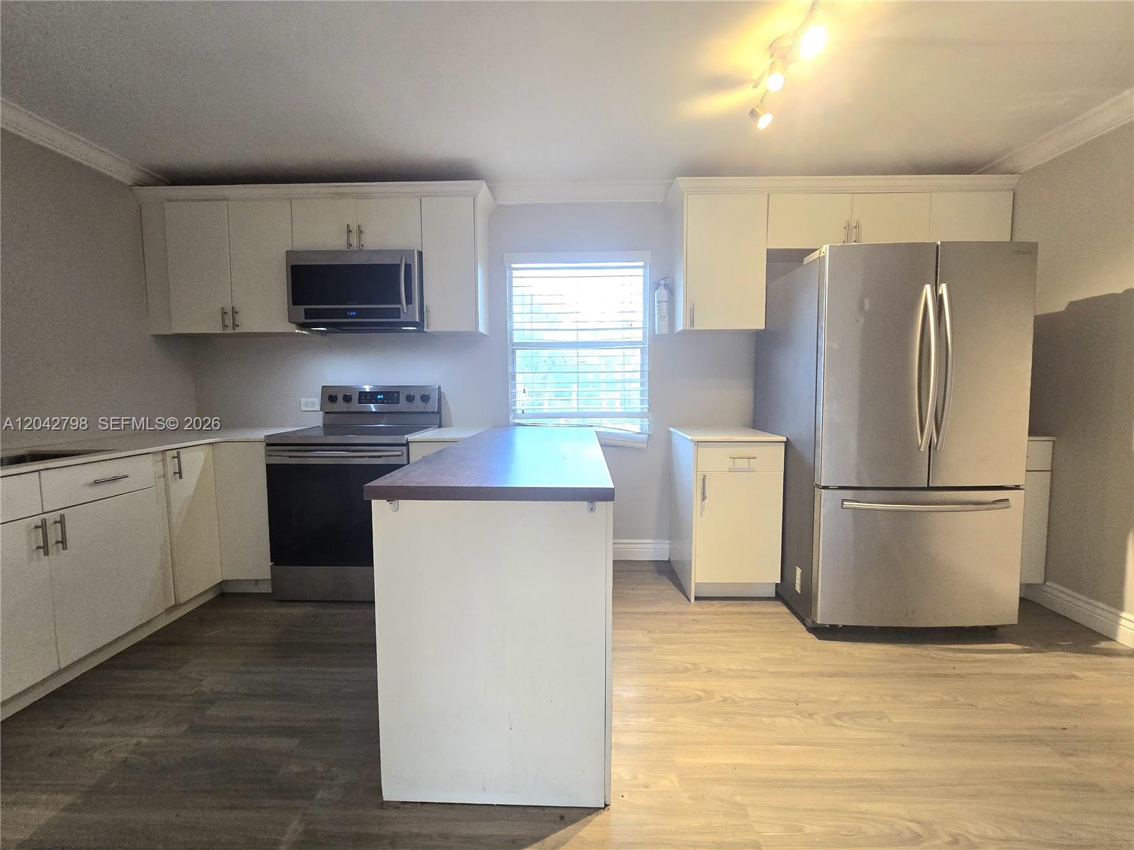 A kitchen features white cabinets, stainless steel appliances, a center island, and wood-look flooring — 914 SW 8th Avenue # 57, Gainesville FL 32601, GAINESVILLE, FL