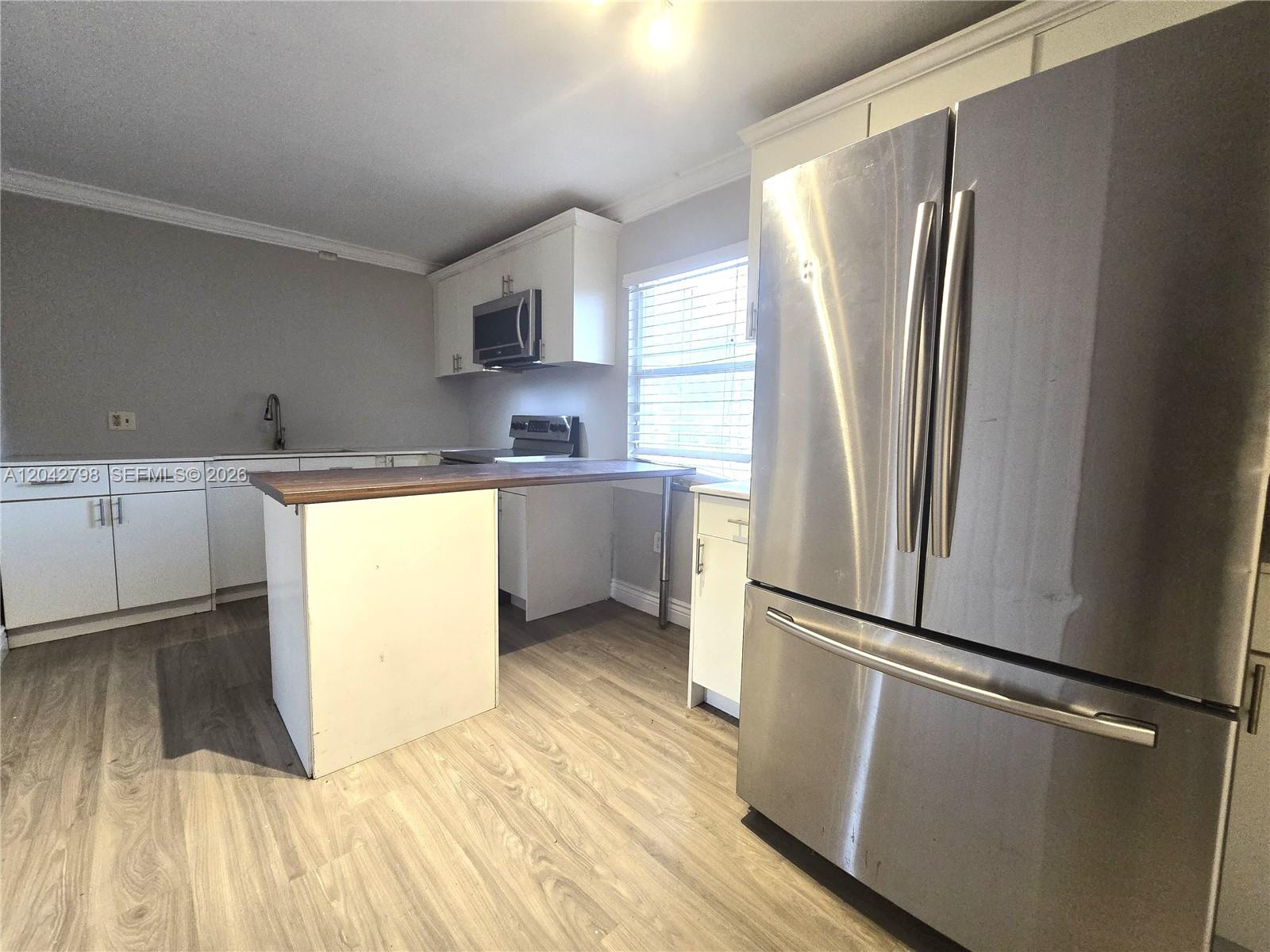 A kitchen features white cabinets, stainless steel appliances, a wood-topped island, and light wood flooring — 914 SW 8th Avenue # 57, Gainesville FL 32601, GAINESVILLE, FL