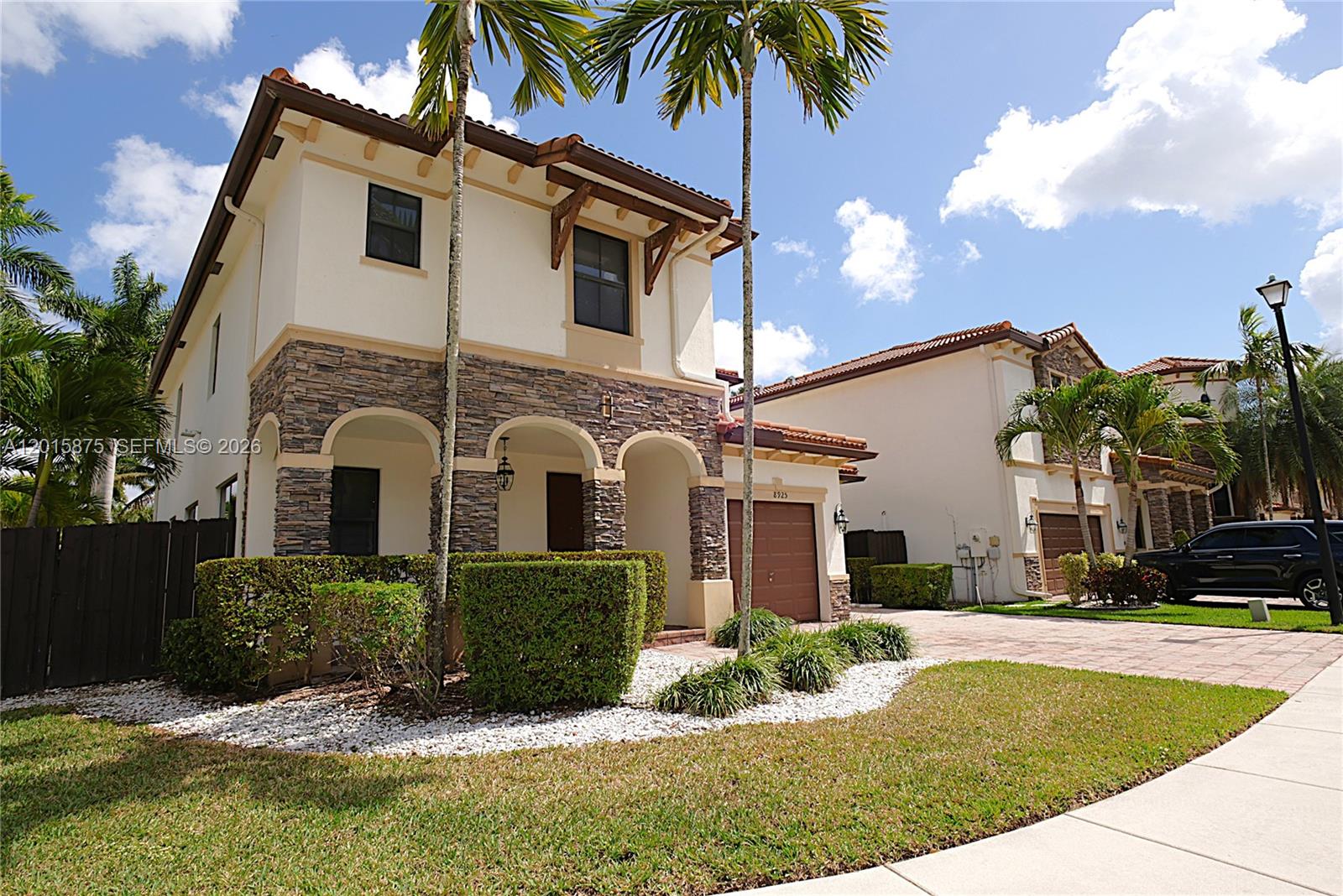 A two-story stucco and stone townhouse features arched entryways, a garage, and palm trees — 8925 NW 99th Ave, Doral FL 33178, DORAL, FL