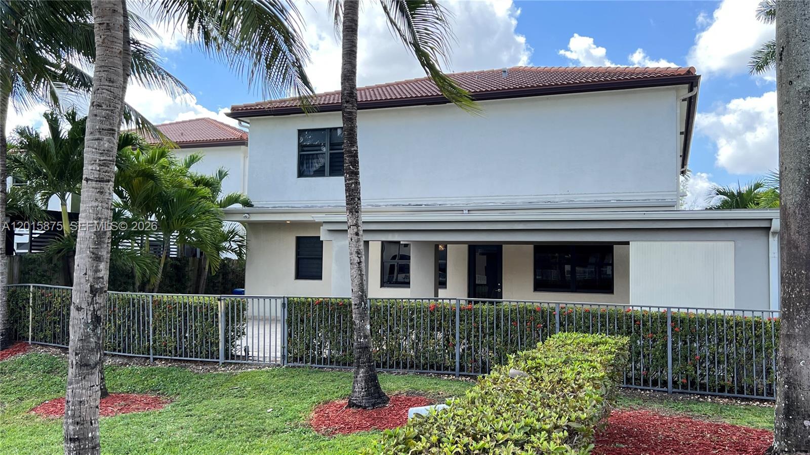 The exterior of a two-story house features a metal fence, palm trees, and landscaping — 8925 NW 99th Ave, Doral FL 33178, DORAL, FL