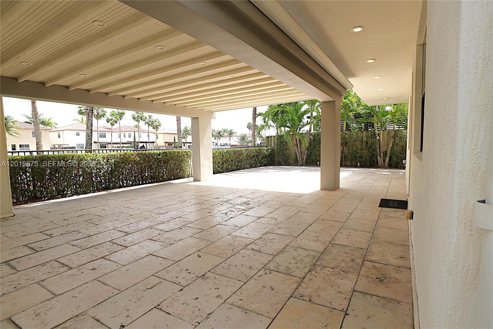 A covered patio features light-colored stone flooring and a view of a landscaped backyard — 8925 NW 99th Ave, Doral FL 33178, DORAL, FL