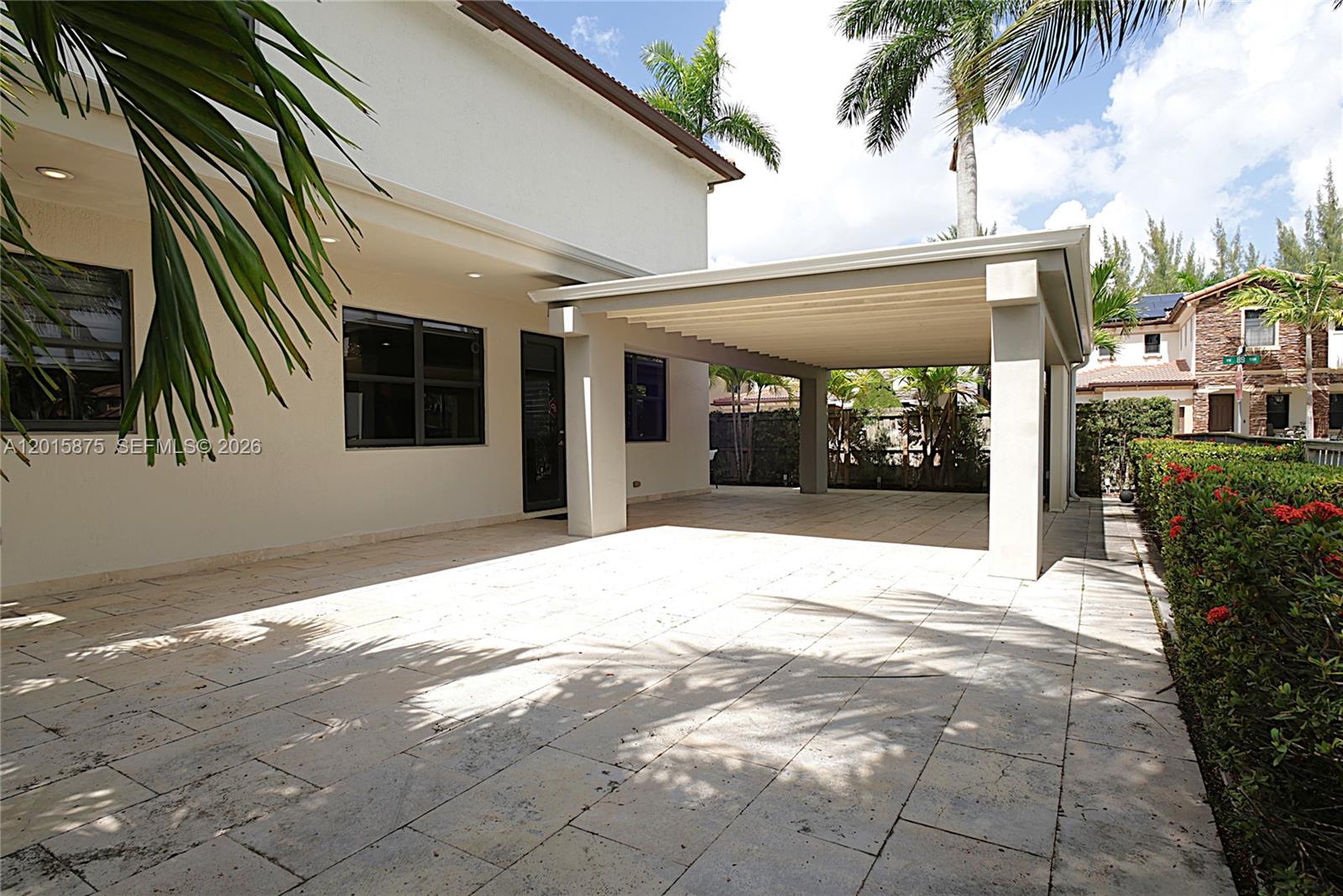 A paved patio area features a covered carport structure attached to a white house — 8925 NW 99th Ave, Doral FL 33178, DORAL, FL