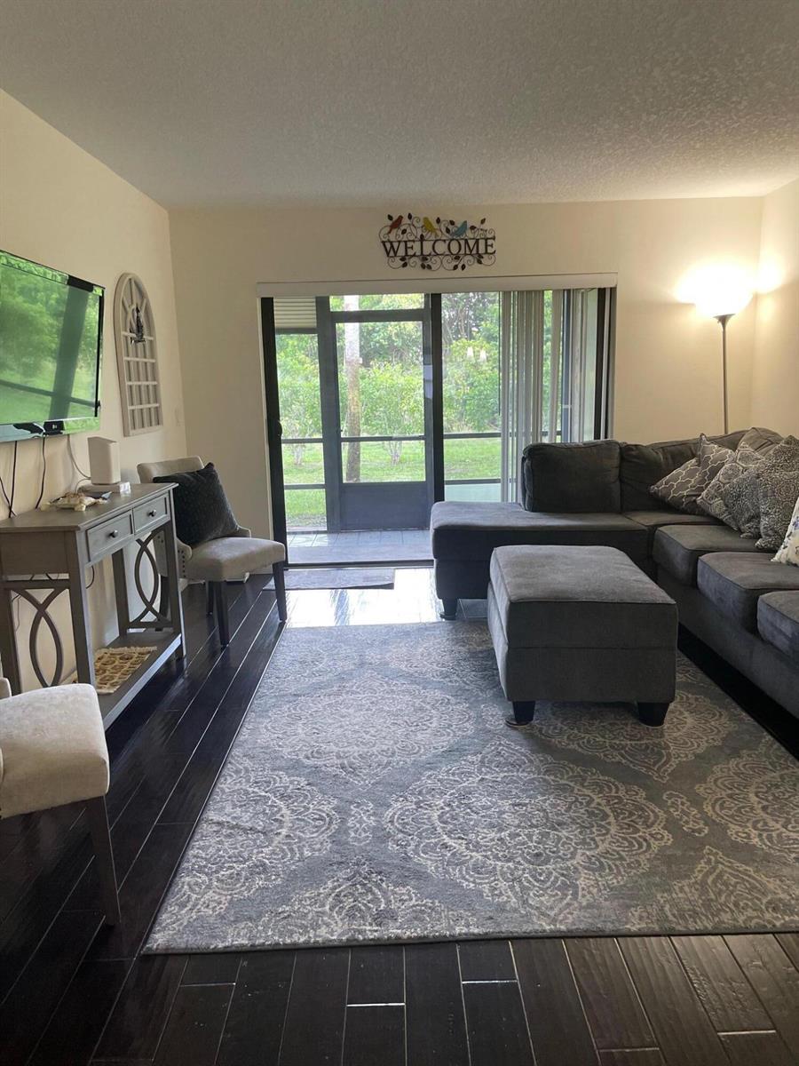 A living room features dark wood floors, a gray sectional sofa, and a sliding glass door — 7879 Willow Spring Circle # 913, Lake Worth FL 33467, LAKE WORTH, FL