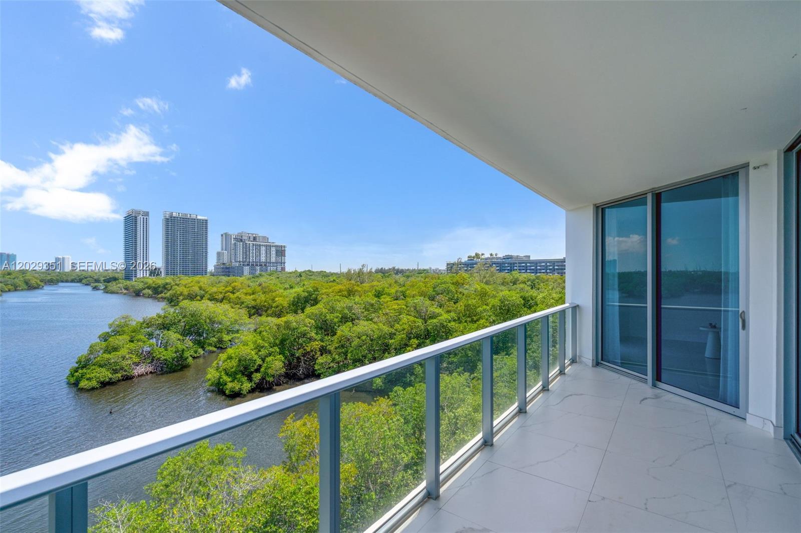 A balcony with white tile flooring overlooks a river and a dense forest of trees — 17111 BISCAYNE BL # 506, North Miami Beach FL 33160, NORTH MIAMI BEACH, FL